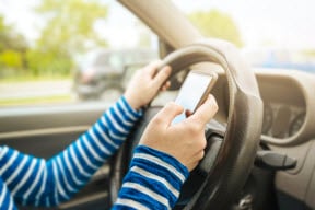 Teen driving holding steering wheel and texting on cell phone