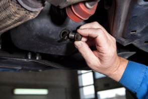 Mans hand holding oil plug near drain opening
